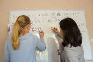 A student writes Chinese on a whiteboard beside a teacher