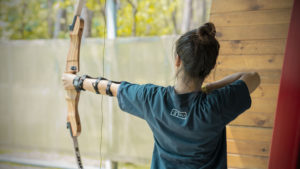 A woman aims a bow at an archery range, seen from behind