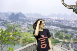 A woman in a CLI shirt stands at an overlook above Guilin