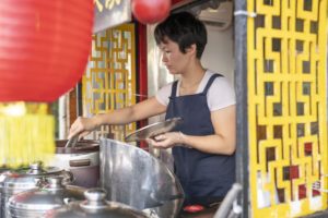 A woman cooks at a street food stall framed by a red lantern