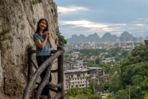 A woman leans against a rock above a view of Guilin and karst peaks