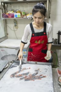 A cook spreads rice batter and minced meat on a steel tray for rice noodle rolls