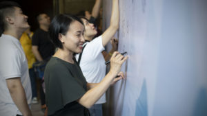Guests sign their names on a white wall with markers