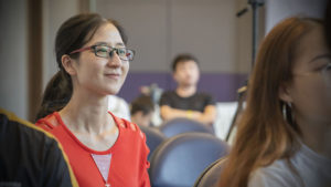 A woman in glasses smiles from her seat in the audience