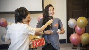 A woman speaks into a microphone beside a CLI prize box and balloons