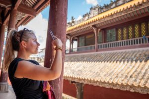 A woman takes a phone photo beside the eaves of a traditional temple