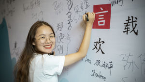 A smiling woman writes on an event signing wall
