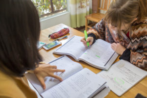 Hands, textbooks and an open workbook spread across a study table
