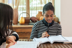 A student reads an open textbook at a table by the window