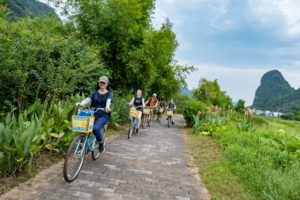 A group cycles along a countryside path past karst hills