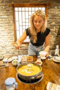 A woman stirs a pot of yellow broth at a hot pot table