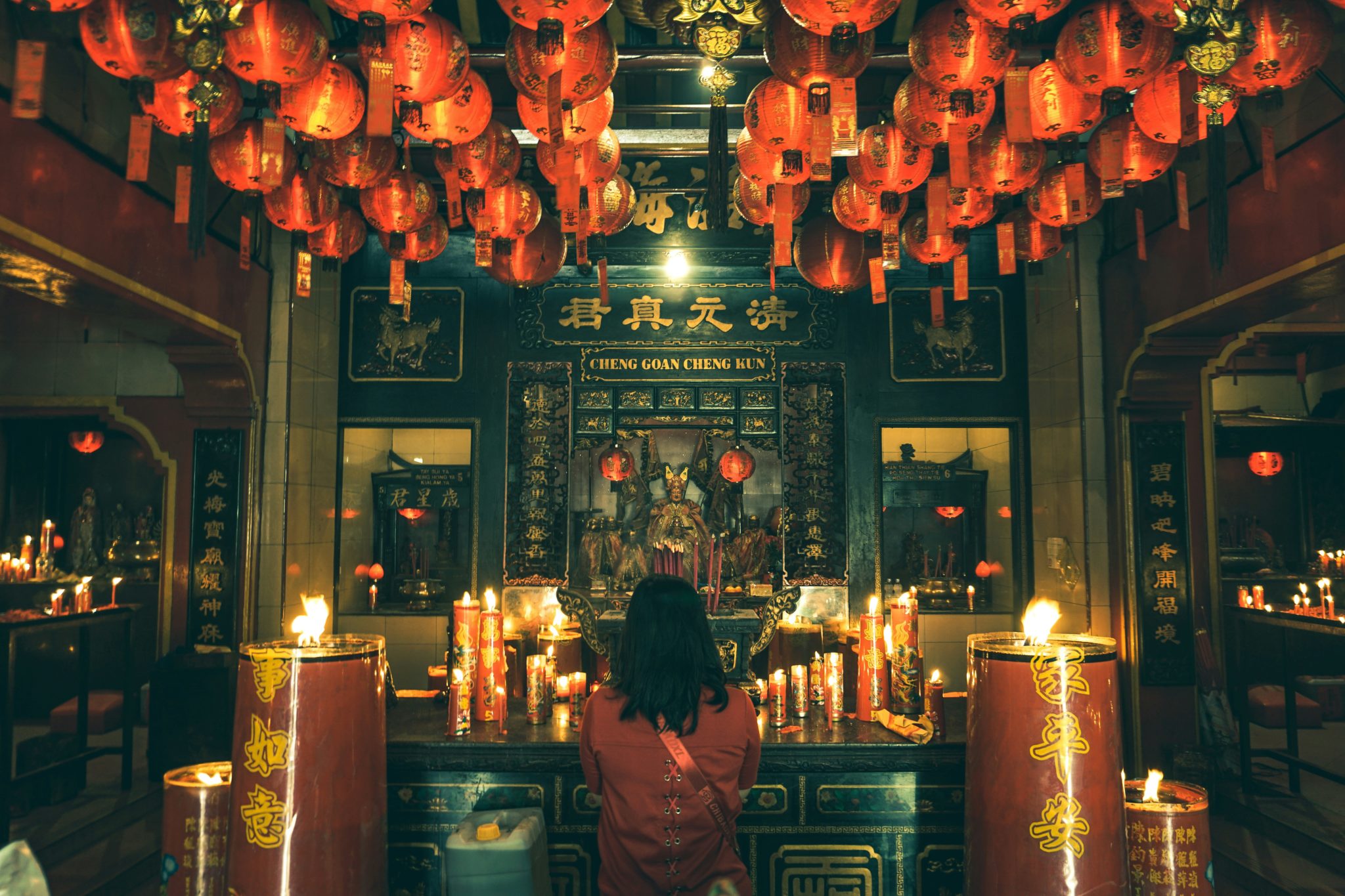 A woman praying before a candlelit altar inside a Daoist temple in Indonesia, surrounded by red lanterns