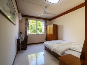 A bright bedroom with a bed, wardrobe, fan and window