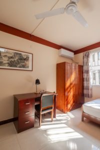 A student room with a wooden desk, wardrobe and bed by the window