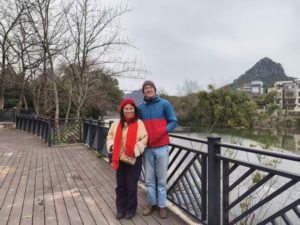A woman in a red scarf and a man pose on a riverside boardwalk