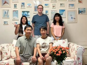 Five people pose by a floral sofa in a room with framed pictures
