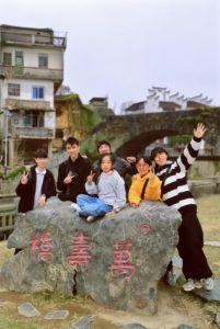 A group poses on a carved stone in a village by an old bridge