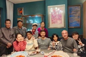 A large group smiles and flashes peace signs around a dinner table at home