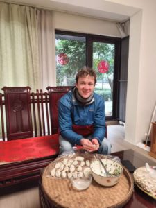 A man smiles at a round table with trays of homemade dumplings