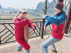Two people in red jackets practice tai chi on a terrace above karst hills