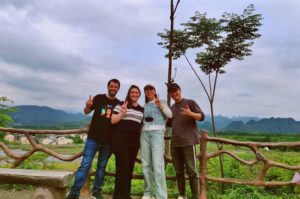 Four people pose by a wooden fence above green countryside