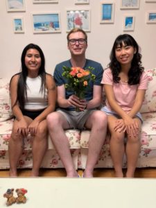 A man holding flowers sits on a floral sofa between two women