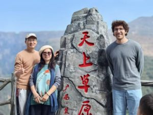 Three people pose beside a carved stone marker on a mountain lookout