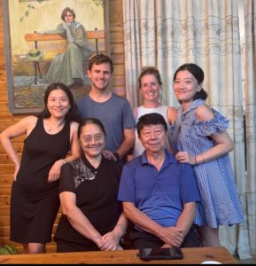 Six people pose at home in front of a painting of a woman on a bench