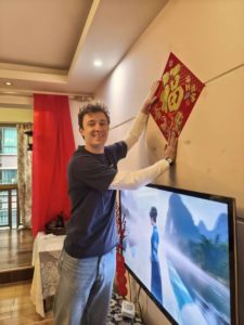 A man hangs a red fu character decoration above a TV at home