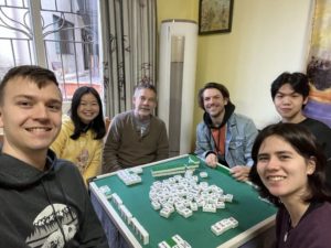 A man takes a selfie with five people around a mahjong table