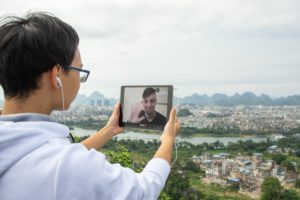 A student holds a tablet on a video call above a view of the city