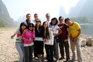 A group poses on a pebble riverbank with misty karst peaks behind