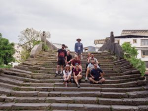 A group sits and stands on wide old stone steps in a village