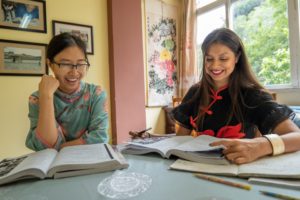 Two women laugh while studying textbooks at a table