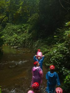 People in colorful ponchos and helmets wade up a forest stream