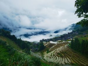 Clouds drift over a mountain valley above rice terraces and a wooden village