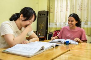 A teacher and student laugh together over open textbooks