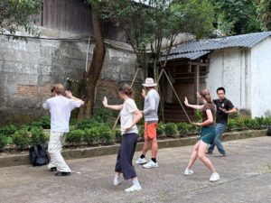 Students follow a tai chi teacher's movements in a paved courtyard