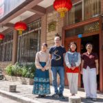 Four people stand outside a brick building's wooden door under red lanterns, house number 31 above