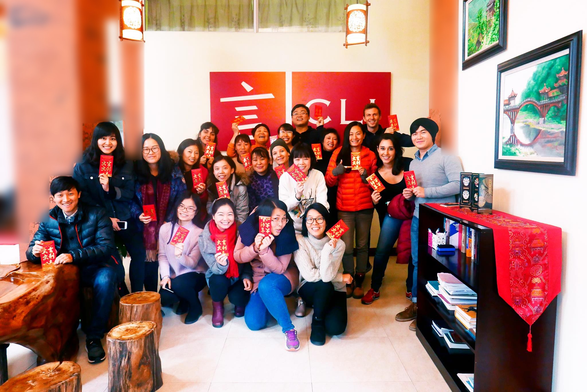 Students and teachers holding red packets in front of the CLI logo wall at the CLI Center in Guilin