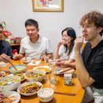 Four people share a meal of many dishes around a round table in a family home