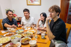 Four people share a meal of many dishes around a round table in a family home