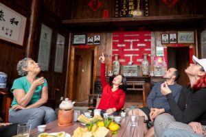 A woman in red points up toward the rafters as the group around a tea table looks up