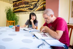 A student runs a finger along a textbook page while his teacher listens at a table with a pen cup