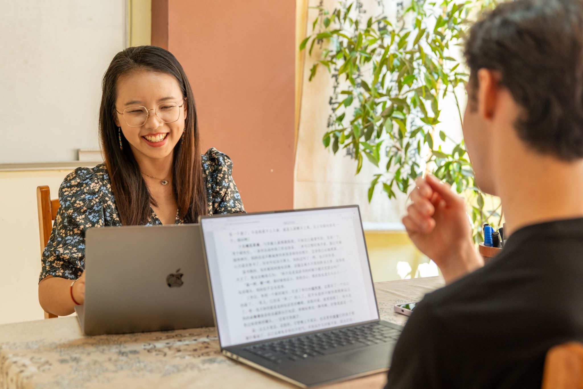 A CLI teacher smiling across the table during a one-on-one lesson, laptops open between her and her student