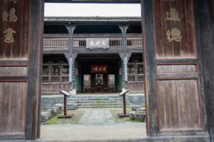 An old wooden gateway frames a courtyard and a two-story ancestral hall with carved plaques